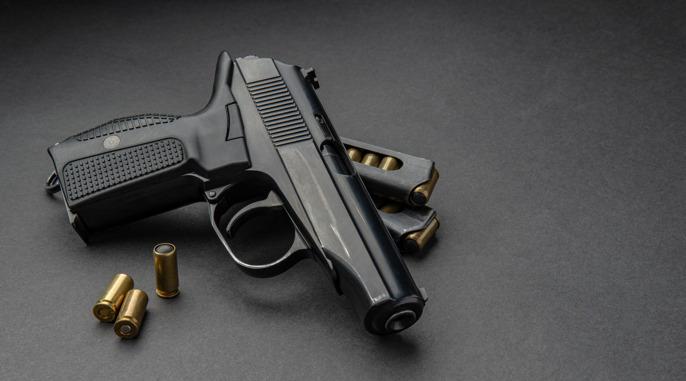 A gun laying on table with two bullets next to it