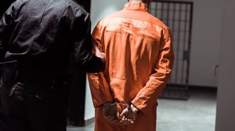 Man in orange jumpsuit being led to jail cell