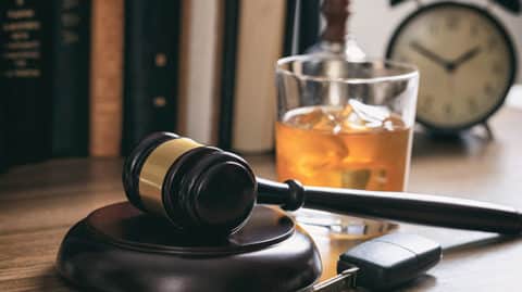 Glass of amber alcohol next to car keys and gavel