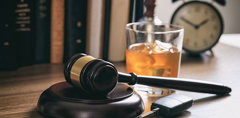 Glass of amber alcohol next to car keys and gavel