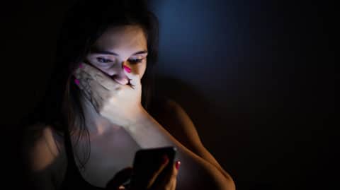 Shocked woman looking at her phone in dark room