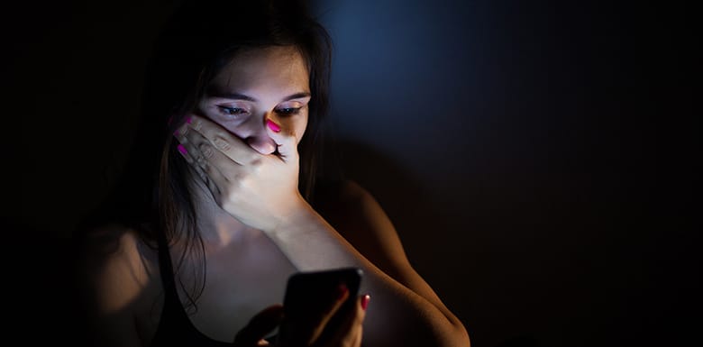 Shocked woman looking at her phone in dark room