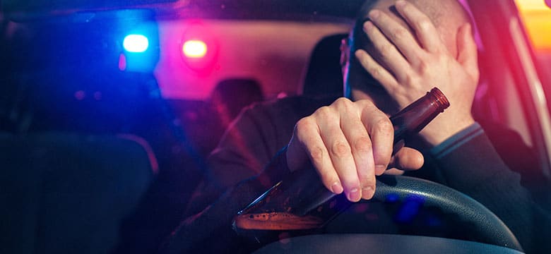 Driver holding beer with police lights in background image