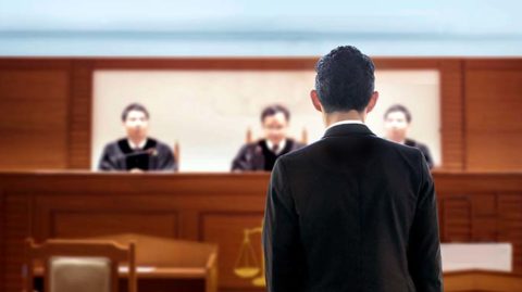 Man in suit speaking to a panel of three judges