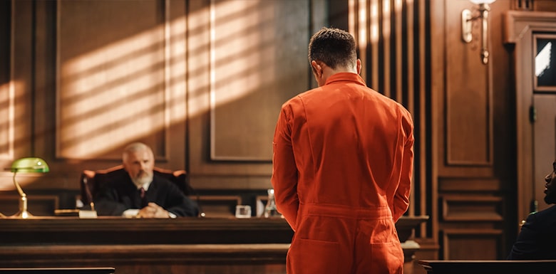 Man in orange jumpsuit facing judge in courtroom during criminal trial
