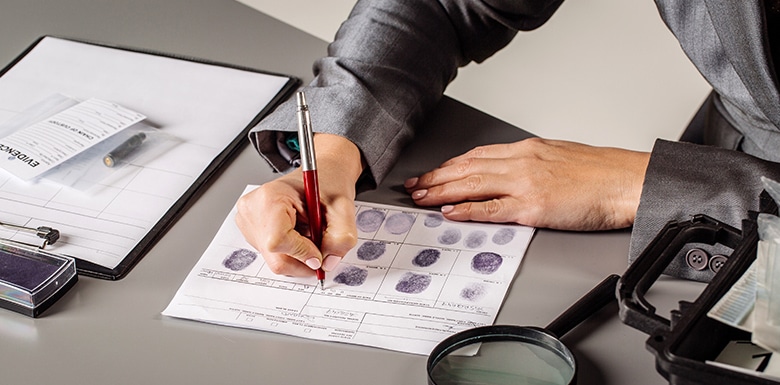 Woman writing notes on fingerprint paperwork with other case evidence on the table