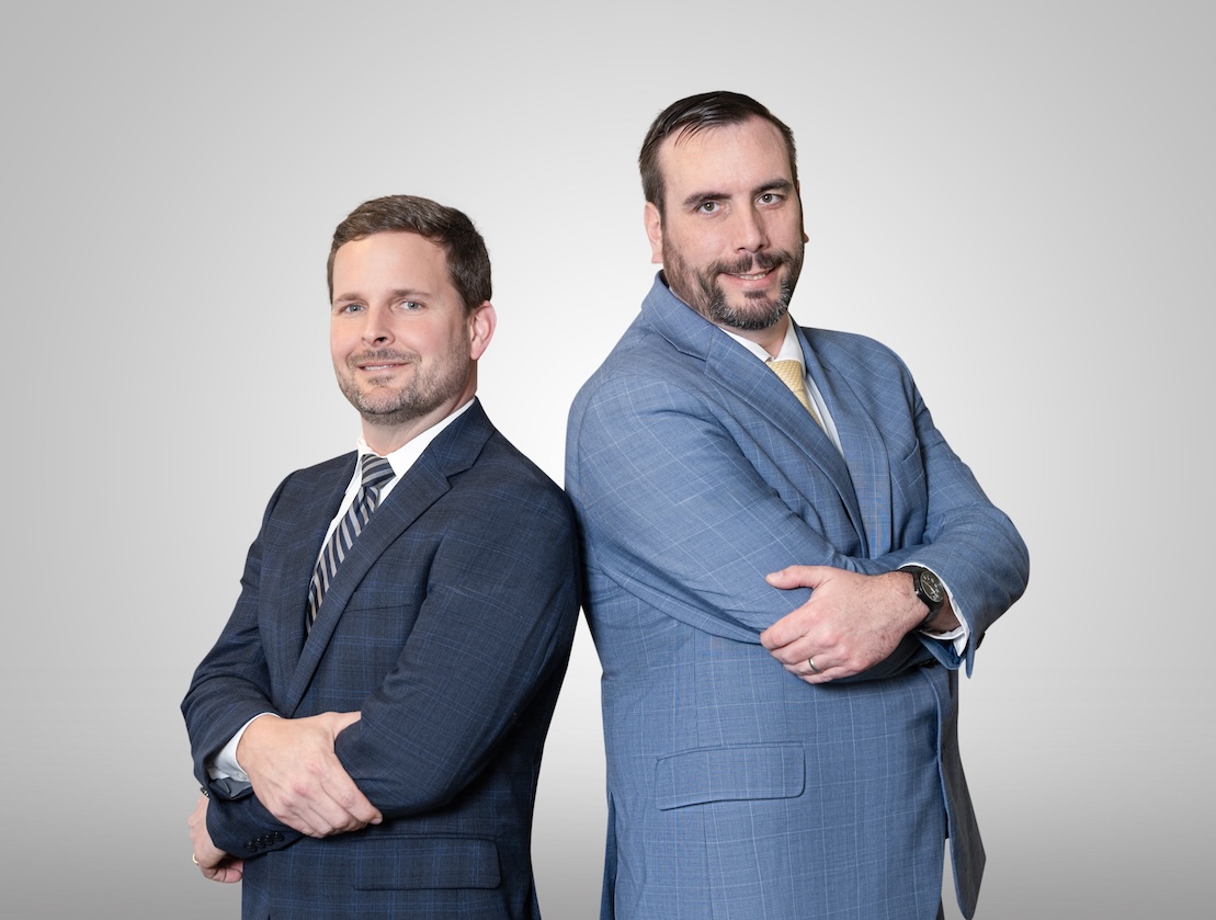 Brad and Robert standing side by side with their backs together, smiling and looking at the camera